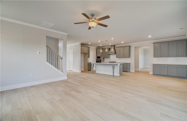 unfurnished living room featuring baseboards, crown molding, light wood finished floors, and stairs