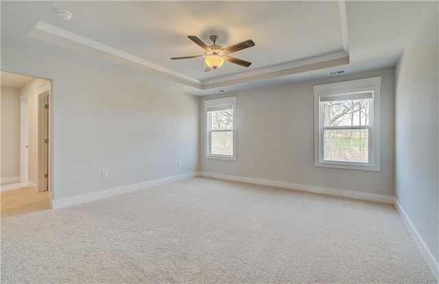 spare room with ceiling fan, light carpet, visible vents, baseboards, and a raised ceiling