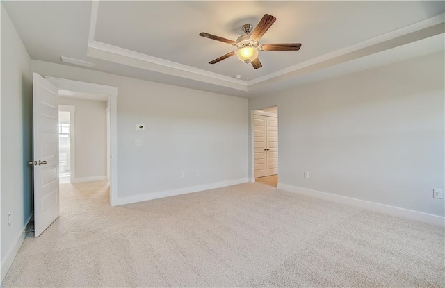 unfurnished room with a ceiling fan, a tray ceiling, light carpet, and baseboards