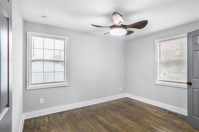 unfurnished room with dark wood-style floors, visible vents, baseboards, and a ceiling fan