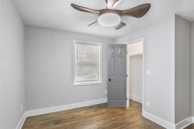 unfurnished bedroom featuring dark wood-style flooring, visible vents, a spacious closet, ceiling fan, and baseboards