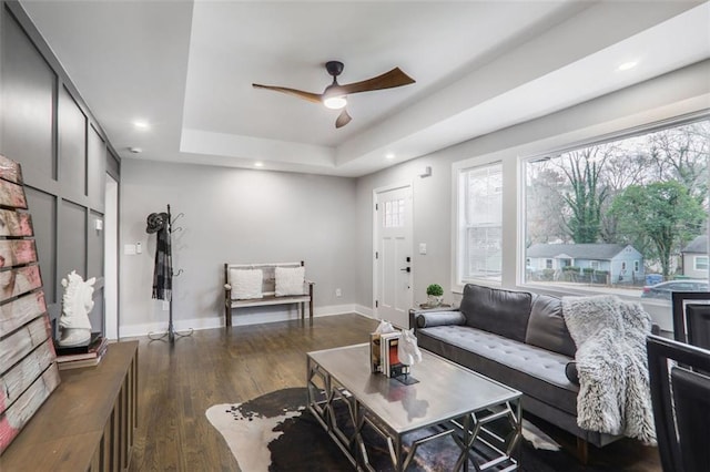 living room featuring a tray ceiling, dark wood-type flooring, recessed lighting, and baseboards