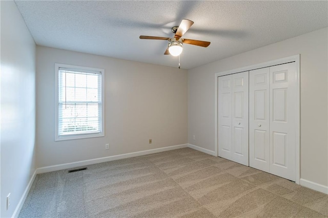 unfurnished bedroom featuring ceiling fan, a closet, light colored carpet, and a textured ceiling