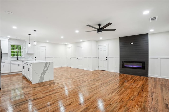 3455 Broxton Mill Way, Snellville, GA 30039 - unfurnished living room with a decorative wall, light wood finished floors, a ceiling fan, a wainscoted wall, and a fireplace