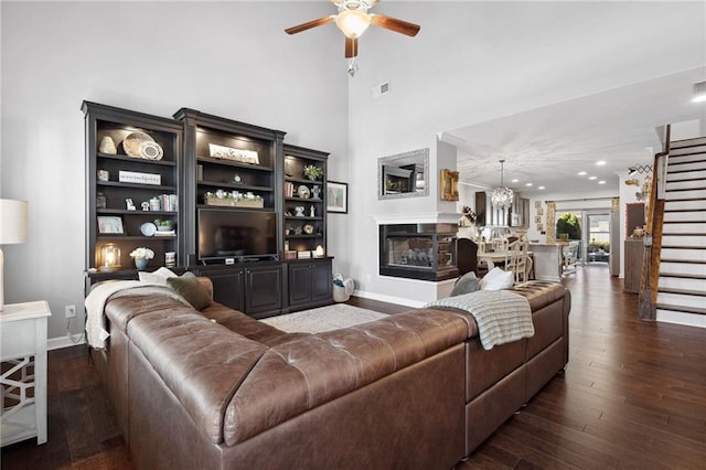 living area featuring dark wood finished floors, visible vents, ceiling fan, a multi sided fireplace, and stairs