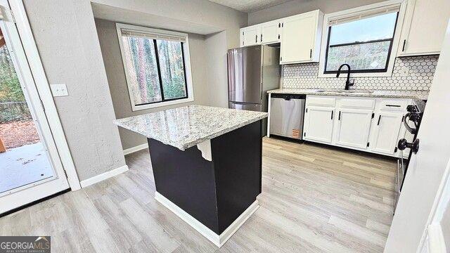 kitchen featuring white cabinetry, stainless steel appliances, backsplash, light stone countertops, and sink