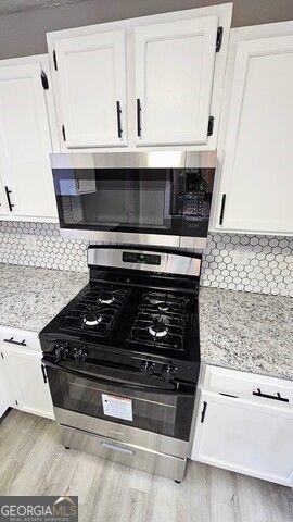 kitchen with appliances with stainless steel finishes, backsplash, light wood-type flooring, light stone countertops, and white cabinets