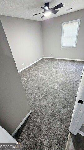 unfurnished room with ceiling fan, a textured ceiling, and dark colored carpet