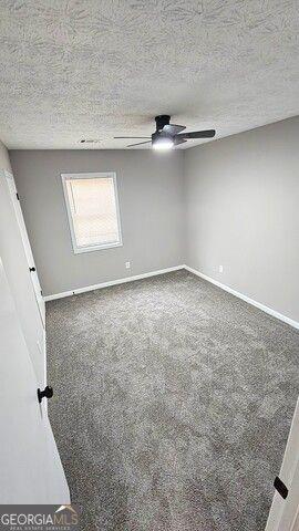 empty room with a textured ceiling, ceiling fan, and dark colored carpet