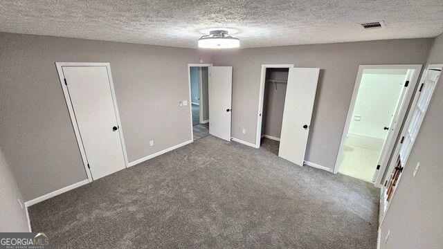 unfurnished bedroom with carpet floors, a textured ceiling, and ensuite bath