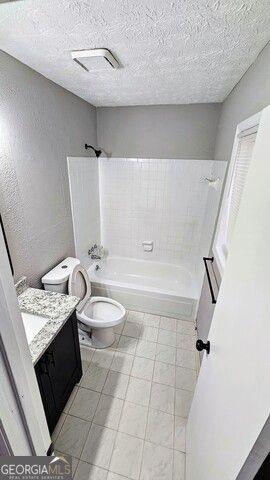 full bathroom featuring toilet, vanity, tiled shower / bath combo, and a textured ceiling