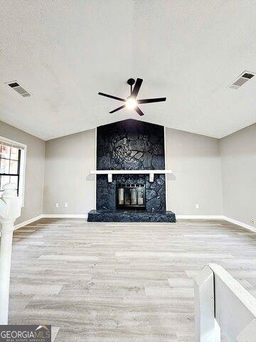 unfurnished living room with ceiling fan, vaulted ceiling, hardwood / wood-style flooring, and a fireplace