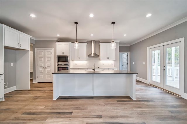 kitchen featuring white cabinets, appliances with stainless steel finishes, wall chimney range hood, and ornamental molding