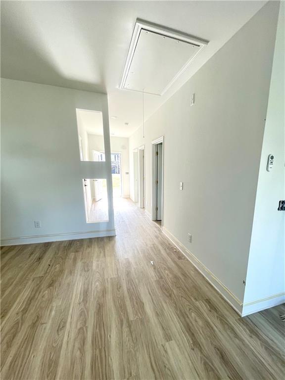 unfurnished room featuring baseboards, wood finished floors, and attic access