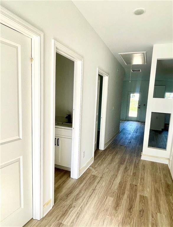 hallway with baseboards, wood finished floors, and attic access