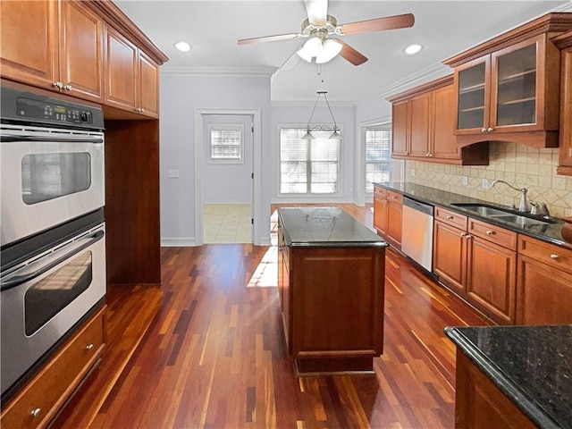 kitchen featuring appliances with stainless steel finishes, ornamental molding, sink, dark stone countertops, and a kitchen island