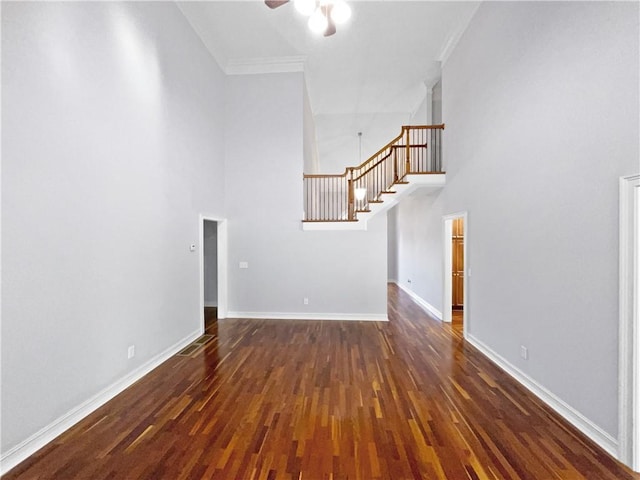 unfurnished living room with a towering ceiling, dark hardwood / wood-style flooring, ceiling fan, and ornamental molding