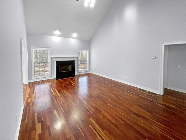 unfurnished living room with plenty of natural light, dark wood-type flooring, and high vaulted ceiling