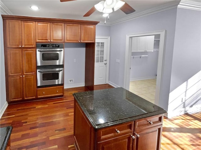 kitchen with dark stone counters, ornamental molding, double oven, ceiling fan, and dark hardwood / wood-style floors