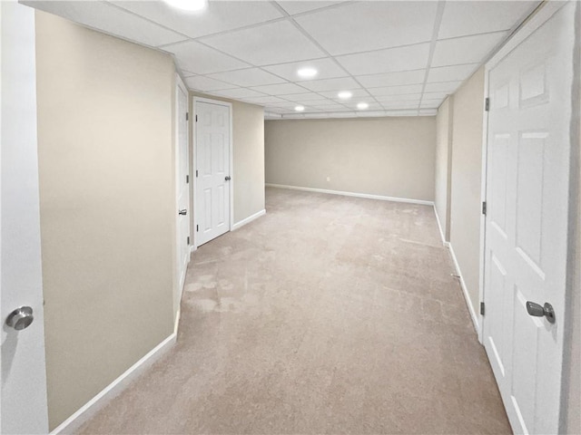 basement with a paneled ceiling and light colored carpet