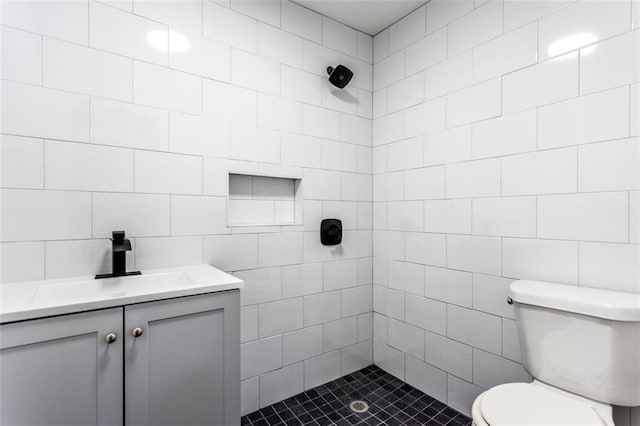 bathroom with a tile shower, vanity, tile walls, and toilet