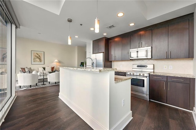 kitchen with hanging light fixtures, stainless steel appliances, a center island with sink, dark hardwood / wood-style flooring, and decorative backsplash