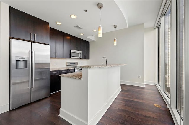 kitchen featuring decorative light fixtures, an island with sink, light stone counters, stainless steel appliances, and dark wood-type flooring