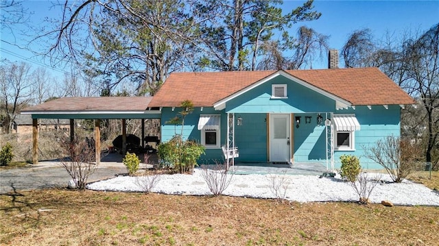 view of front of house featuring driveway, a carport, and a chimney