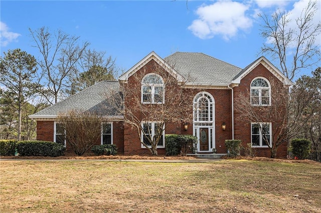 view of front facade featuring brick siding, a front lawn, and roof with shingles