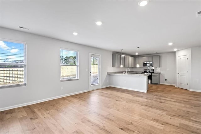 kitchen with light hardwood / wood-style flooring, stainless steel appliances, decorative light fixtures, gray cabinets, and kitchen peninsula