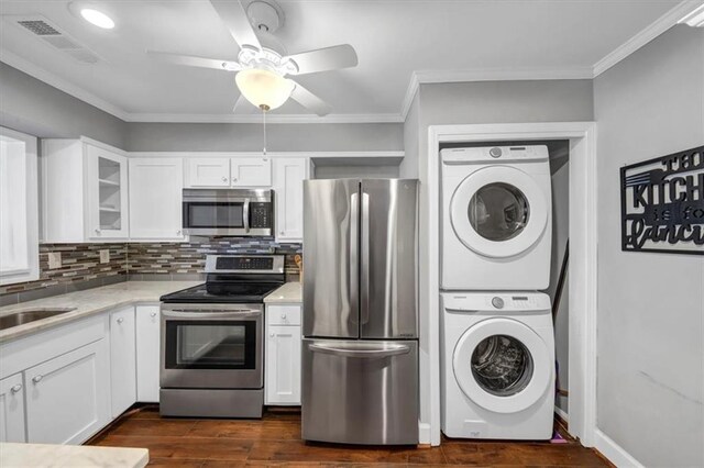 kitchen with crown molding, appliances with stainless steel finishes, white cabinetry, stacked washer / drying machine, and dark hardwood / wood-style floors