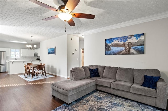 living room with ceiling fan with notable chandelier, a textured ceiling, dark hardwood / wood-style floors, and ornamental molding