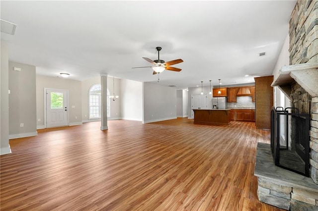 unfurnished living room with a fireplace, a ceiling fan, baseboards, light wood-type flooring, and decorative columns