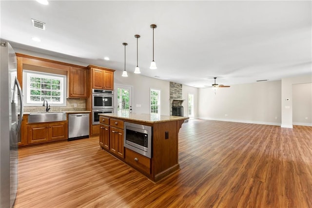kitchen with appliances with stainless steel finishes, a sink, brown cabinetry, light wood-style floors, and a stone fireplace