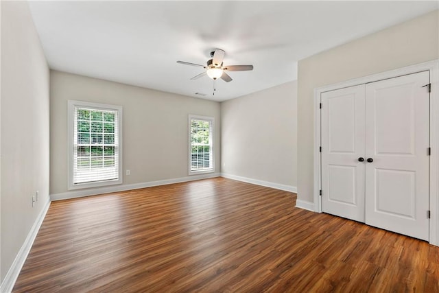 unfurnished bedroom with wood finished floors, multiple windows, baseboards, and ceiling fan
