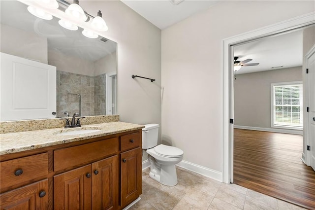 bathroom featuring a tile shower, baseboards, vanity, ceiling fan, and toilet