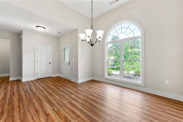 spare room featuring wood finished floors, healthy amount of natural light, baseboards, and a chandelier