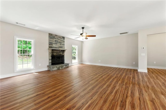 unfurnished living room with ceiling fan, wood finished floors, a stone fireplace, and baseboards