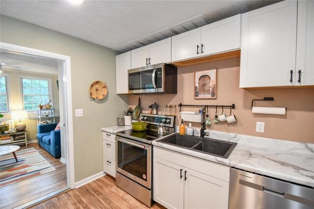 1235 Riverside Dr Unit H3, Gainesville, GA 30501 - kitchen featuring stainless steel appliances, light wood-style flooring, white cabinets, a sink, and light stone countertops