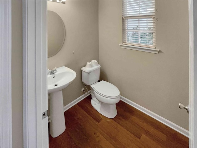 half bath with a sink, toilet, baseboards, and wood finished floors