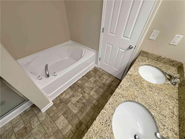 full bath featuring double vanity, stone finish flooring, a bath, and a sink