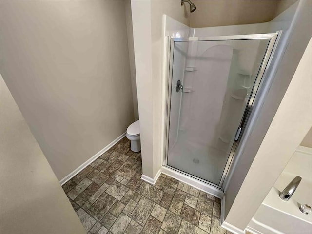 full bathroom with a shower stall, toilet, stone finish flooring, and baseboards