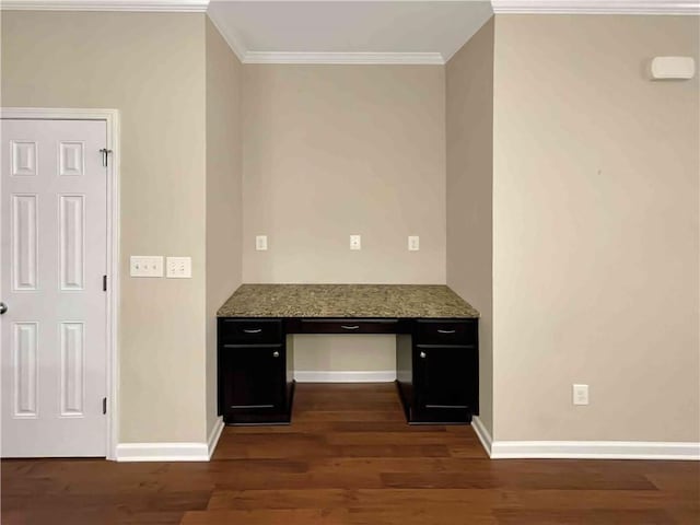 unfurnished office featuring dark wood finished floors, built in desk, crown molding, and baseboards