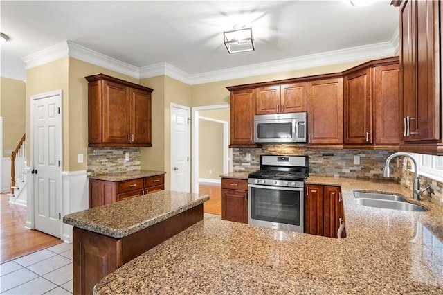 kitchen featuring appliances with stainless steel finishes, light stone countertops, light wood-type flooring, ornamental molding, and sink