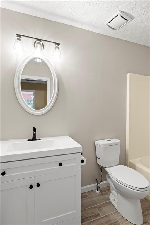 bathroom with a textured ceiling, hardwood / wood-style flooring, vanity, and toilet