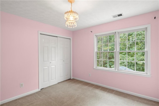 unfurnished bedroom with light colored carpet, a textured ceiling, a closet, and a chandelier