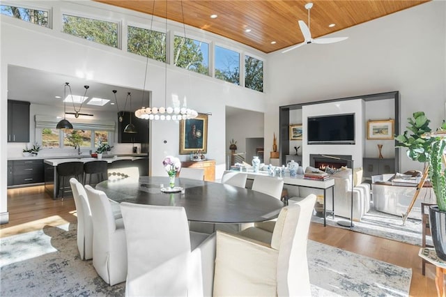 dining room featuring light wood-type flooring, ceiling fan with notable chandelier, a wealth of natural light, and wooden ceiling