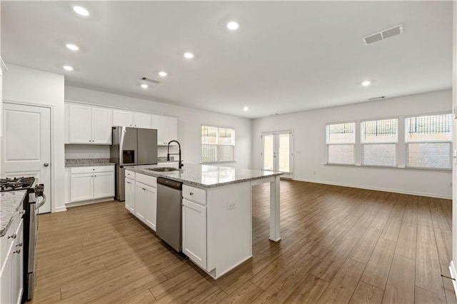 kitchen with stainless steel appliances, wood finished floors, a sink, visible vents, and white cabinetry