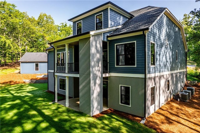 rear view of property with a lawn, a balcony, stucco siding, cooling unit, and a shingled roof