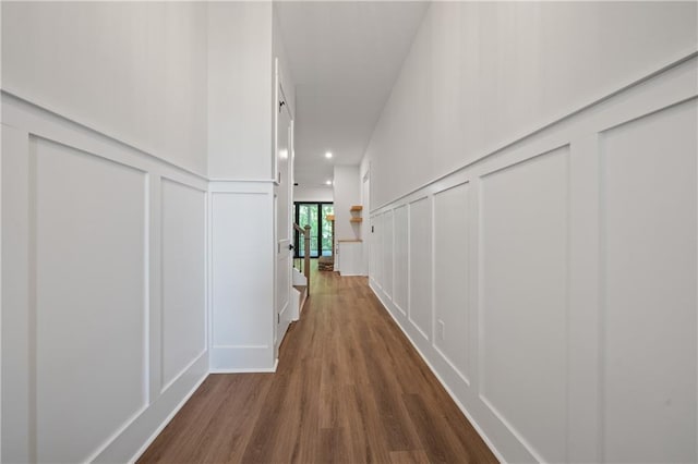 hall featuring a decorative wall, recessed lighting, dark wood-type flooring, and a wainscoted wall